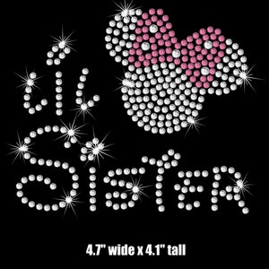 May include: Rhinestone iron-on design featuring the words "Big Sister" in white rhinestones and a pink and white heart with a bow. The design measures 4.7 inches wide by 4.1 inches tall.