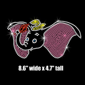 May include: Pink rhinestone iron-on design of an elephant with a yellow hat. The design is 8.6 inches wide and 4.7 inches tall.