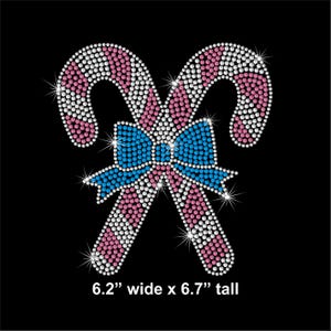 May include: A rhinestone design of two candy canes with a blue bow, set against a black background. The candy canes are pink and white, and the bow is blue. The text at the bottom reads: 6.2" wide x 6.7" tall.