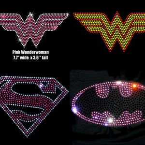 May include: Four iron-on rhinestone patches featuring superhero logos. The patches are pink, yellow, and black with red accents. The logos are Wonder Woman, Superman, and Batman. The Wonder Woman patch is 7.7 inches wide by 3.6 inches tall.