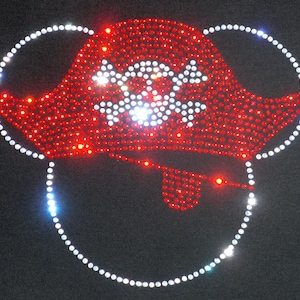 May include: Red and white rhinestone design of a pirate hat and eye patch on a black background.