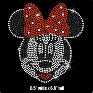 May include: A rhinestone design of a cartoon character's face with a red bow. The face is made of white rhinestones, outlined in black rhinestones, and has a red mouth. The bow is red with white rhinestone accents. The design is 6.5" wide x 6.8" tall.