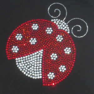 May include: Red and white ladybug design made of rhinestones. The ladybug has a white body with red spots and red wings with white spots. The ladybug has two antennae.