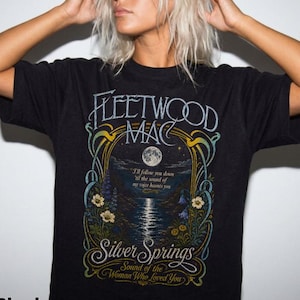 May include: A black short-sleeve t-shirt featuring a graphic print with the text Fleetwood Mac, Silver Springs, and the lyrics I'll follow you down 'til the sound of my voice haunts you and Sound of the Woman Who Loved You, with a moonlit lake scene.