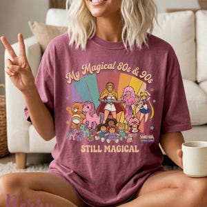 May include: A maroon t-shirt with a graphic featuring cartoon characters from the 80s and 90s, including Care Bears, My Little Pony, and Sailor Moon. The text reads "My Magical 80s & 90s STILL MAGICAL".