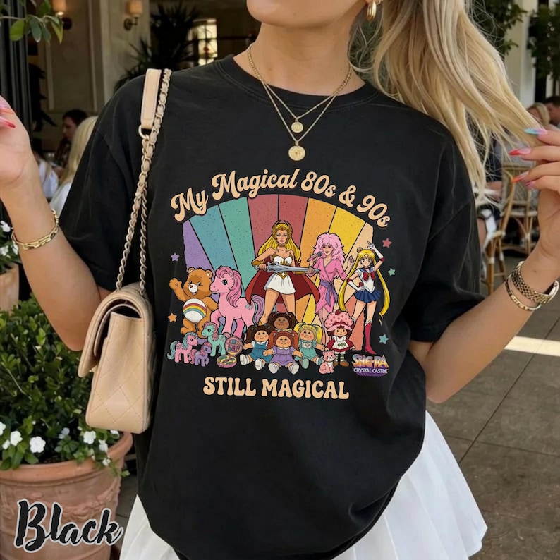 May include: Black t-shirt with a colorful graphic featuring cartoon characters from the 80s and 90s, including Care Bears, My Little Pony, and Sailor Moon. The text on the shirt reads "My Magical 80s & 90s STILL MAGICAL."