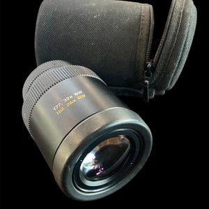 May include: A black camera lens with a black fabric case. The lens has the text "T62 26X WW 177-32X WW" printed on the side.