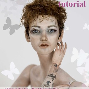 K&ouml;nnte beinhalten: Ein Tutorial f&uuml;r eine Puppenper&uuml;cke mit einer Puppe mit einer kurzen, lockigen, rotbraunen Per&uuml;cke. Die Puppe hat blaue Augen und ein gemaltes Schmetterlings-Tattoo auf dem Arm. Der Text "A Mohair Wig On A Hard Magnetic Base" befindet sich am unteren Rand des Bildes.