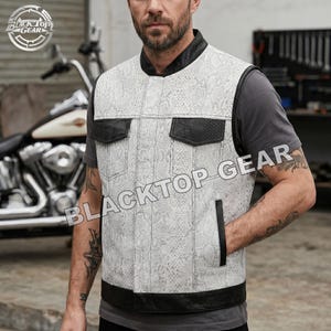 May include: A sleeveless vest featuring a white and gray snakeskin pattern with black leather trim on the collar, pocket flaps, and bottom hem. The vest includes two chest pockets and two side pockets, with the text BLACKTOP GEAR printed across.