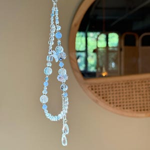 Pu&ograve; includere: Un ornamento di perline fatto a mano con perline trasparenti e azzurro chiaro. Il design include perline rotonde, sfaccettate e a goccia, con un accento floreale. L'ornamento &egrave; appeso a una catena color argento.
