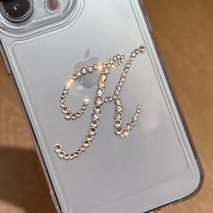 May include: A clear phone case with a sparkly rhinestone letter K on the back.
