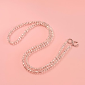 May include: A clear, beaded lanyard with silver-colored metal clasps against a pink background. The lanyard is made of small, faceted beads strung together to create a delicate, sparkling accessory. The design is simple and elegant.