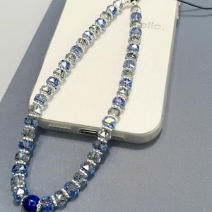 Peut inclure: Un porte-clés de téléphone avec un dégradé de perles de cristal bleu clair et transparentes. Le porte-clés a une perle bleu foncé au bas et une ficelle noire.
