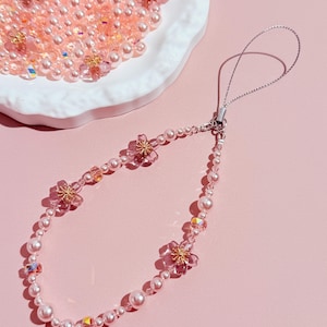 May include: A pink and white beaded phone charm with a silver chain and four pink flower accents.
