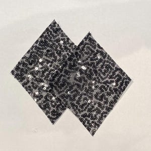 Puede incluir: Dos parches negros en forma de diamante cubiertos de lentejuelas negras.