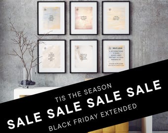 May include: A black and white graphic with the text "TIS THE SEASON SALE SALE SALE BLACK FRIDAY EXTENDED" on a black background. The graphic is over a white table with six framed prints on the wall behind it. The prints are watercolor and feature positive affirmations.