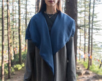 May include: A person wearing a gray and blue wrap jacket with a black shirt and sunglasses. The person is standing in a forest.