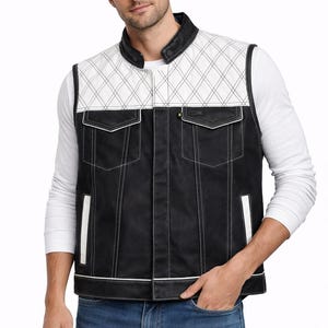 Könnte beinhalten: Eine schwarz-weiße Weste mit einem gesteppten weißen Oberteil und einem schwarzen Unterteil. Die Weste hat zwei Vordertaschen und weiße Paspeln. Das Model trägt ein weißes Langarmshirt und eine blaue Jeans.