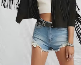 May include: A black suede jacket with long fringe detailing on the sleeves. The jacket is worn over a white crop top and paired with light blue denim shorts. A black belt and silver jewelry complete the look.