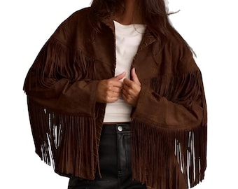 May include: A brown suede jacket with long fringe detailing on the sleeves and chest. The jacket is worn over a white top and paired with black leather pants. The model is wearing black sunglasses.