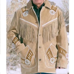 Könnte beinhalten: Hellbraune Wildlederjacke mit Fransen und dekorativen Perlenarbeiten. Die Jacke hat eine Knopfleiste, zwei Vordertaschen und Verzierungen an Schultern und Ärmeln. Die Jacke hat einen klassischen Western-Stil.