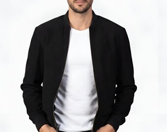 Pode incluir: Casaco bomber preto com fecho de correr, usado sobre uma camiseta branca e jeans pretos. O casaco tem punhos e bainha canelados. A pessoa está de pé com as mãos nos bolsos.