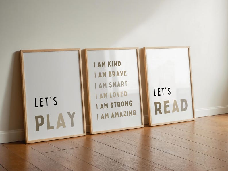 May include: Three framed art prints with positive messages. The first print says "Let's Play" in black and taupe. The second print lists affirmations. The third print says "Let's Read" in black and taupe. The frames are light wood.