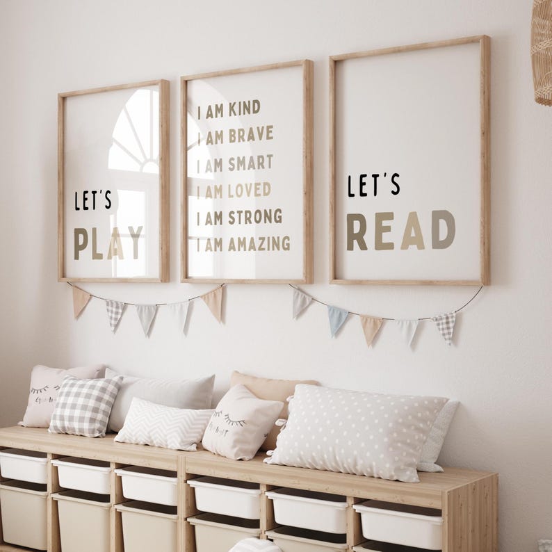 May include: Three framed prints with motivational quotes and the phrases "Let's Play" and "Let's Read". A garland of small flags hangs below the prints. A wooden storage unit with white bins and decorative pillows is below the prints.