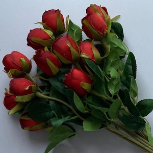 May include: A bouquet of artificial red roses with green leaves and stems. The stems are tied together with twine.