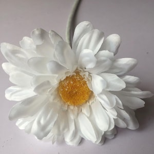 May include: A single white silk flower with a yellow centre. The flower is on a white background.