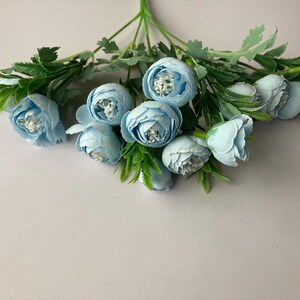 May include: A bouquet of light blue artificial flowers with green stems and leaves.