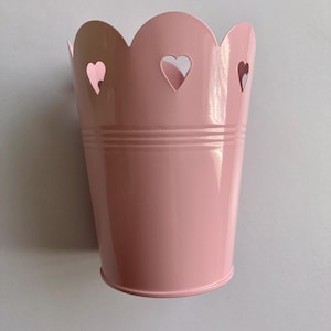 May include: A pink metal planter with a scalloped rim and heart cutouts.