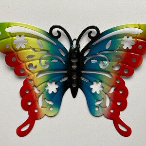 May include: A colourful metal butterfly wall decoration with a rainbow gradient design. The butterfly has intricate cutouts and a black body.
