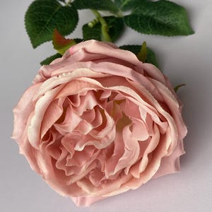 May include: A single, blush pink artificial rose with a green stem and leaves.