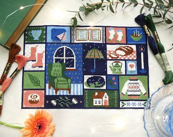 May include: A cozy, cross-stitch sampler featuring a grid of squares with various home-themed images. The squares depict a teacup, boots, an open book, socks, a bowl of food, a window with a chair, an umbrella, bread, a teapot, a candle, a cat, a house, and a sweater.