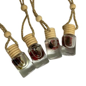 Puede incluir: Cuatro botellas de vidrio con un tapón de corcho natural y un colgador de cuerda marrón. Cada botella contiene flores secas y un líquido transparente. Las botellas cuelgan de la cuerda.