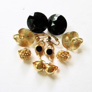 May include: A collection of vintage gold tone earrings with black and white accents. The earrings feature a variety of styles, including clip-on, dangle, and stud.