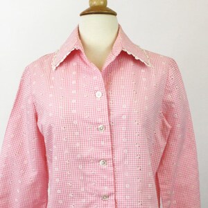 May include: A pink and white gingham button-up shirt with a white lace collar and cuffs. The shirt has a fitted silhouette and a long sleeve.