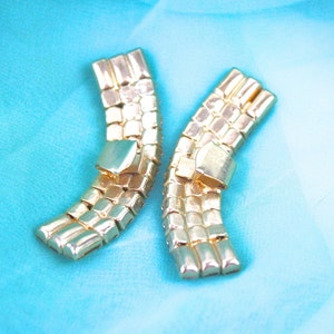 May include: Two gold-tone metal belt buckles with a geometric design. The buckles are curved and have a shiny finish.