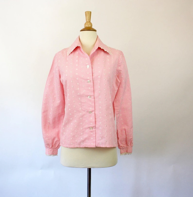 May include: A pink and white gingham button-up shirt with a white lace collar and cuffs. The shirt has a fitted silhouette and long sleeves.