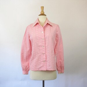 May include: A pink and white gingham button-up shirt with a white lace trim collar and cuffs. The shirt has a long sleeve and a fitted silhouette.
