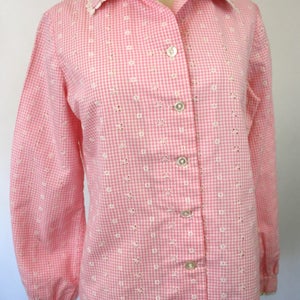 May include: A pink and white gingham button-up shirt with eyelet embroidery and a lace trim collar.