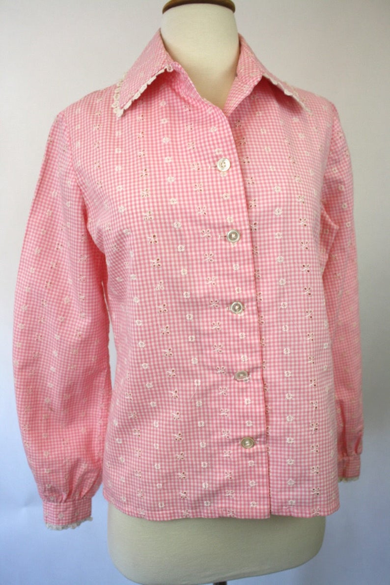 May include: A pink and white gingham button-up shirt with eyelet embroidery and a lace trim collar.