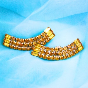 May include: Two gold-toned, curved, rhinestone-encrusted hair clips with amber-colored stones.