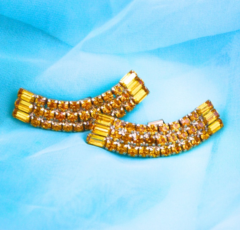 May include: Two gold-toned, curved, rhinestone-encrusted hair clips with amber-colored stones.