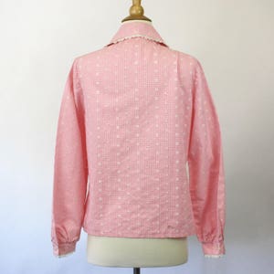 May include: A pink and white gingham long-sleeve shirt with a white lace collar and cuffs. The shirt has a delicate floral pattern.