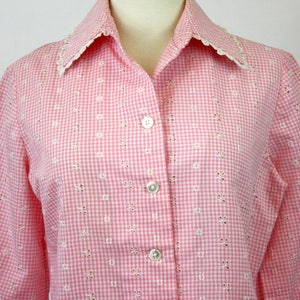 May include: A pink and white gingham button-up shirt with eyelet embroidery and a lace collar.