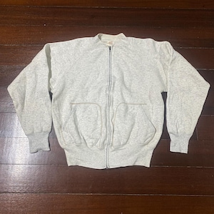 May include: A light gray zip-up sweatshirt with a high collar and two front pockets. The sweatshirt has ribbed cuffs and waistband. The zipper runs down the center of the garment.