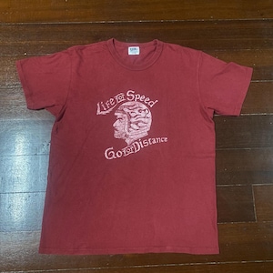 May include: A maroon t-shirt with a graphic design. The design features a helmeted head and the words "Life for Speed" above and "Go for Distance" below. The shirt is made of a soft material.