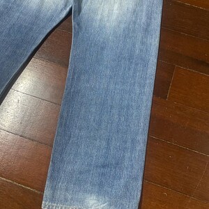 May include: Light blue denim jeans with a faded wash. The jeans have a classic five-pocket design and a straight leg cut. The fabric shows signs of wear and tear, adding to the vintage aesthetic. The jeans are a versatile wardrobe staple.